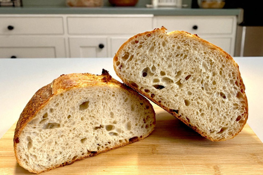 Dos mitades de un pan casero con levadura mostrando una miga abierta sobre una tabla de madera