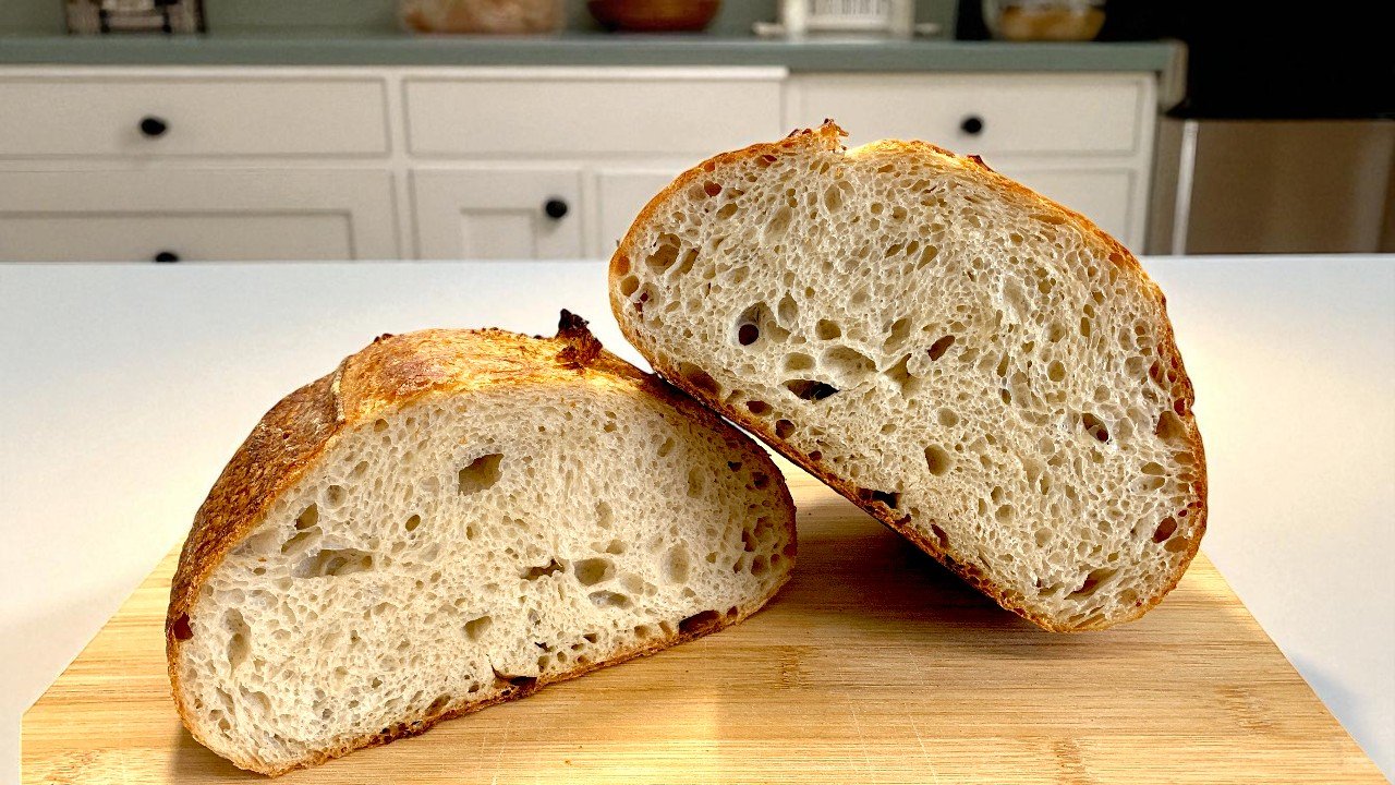 Dos mitades de un pan casero con levadura mostrando una miga abierta sobre una tabla de madera