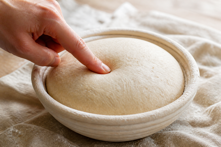 Dedo presionando suavemente una pieza de masa durante la fermentación final