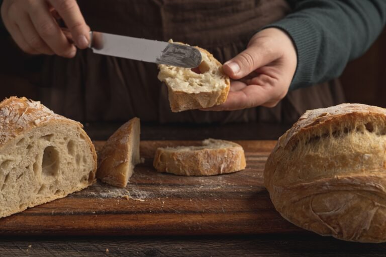 Manos untando mantequilla sobre una rebanada de pan de corteza crujiente