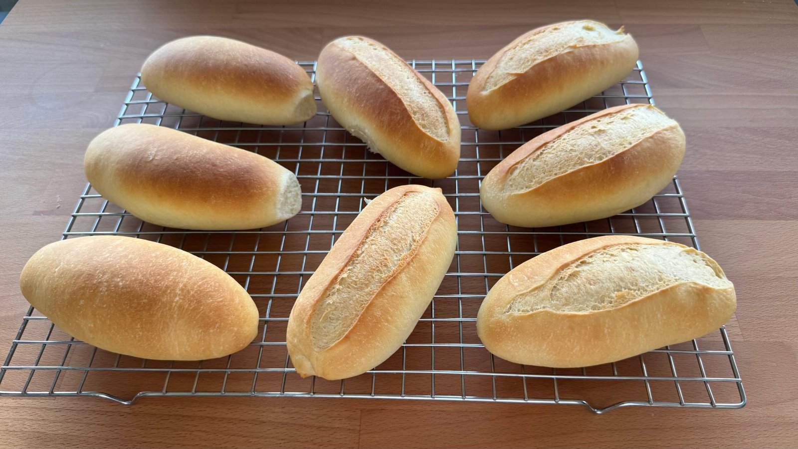 Ocho panecillos caseros dorados, algunos con corte longitudinal, enfriándose sobre una rejilla.