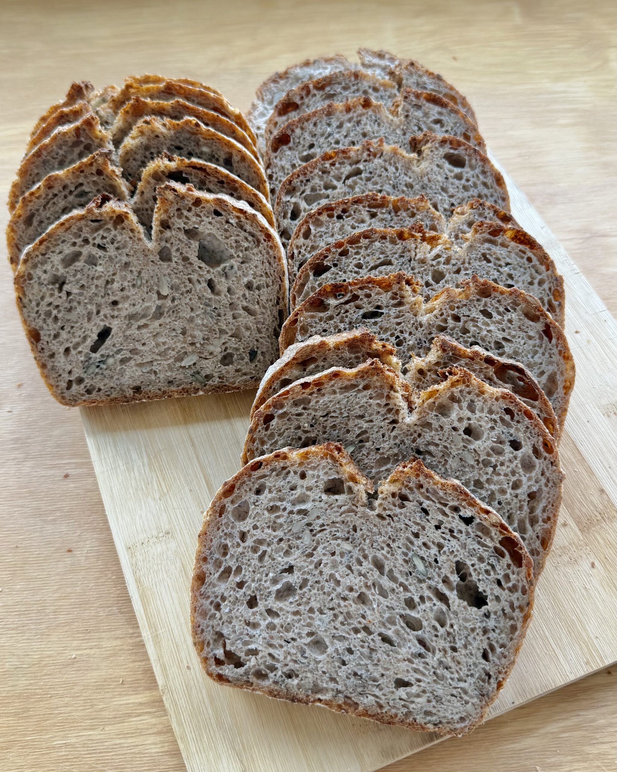 Rebanadas de pan de trigo y centeno con semillas sobre una tabla de madera, mostrando la miga.